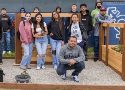 Students and staff at IVA High pose in front of a large raised garden bed in the school's backyard.